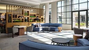 Un área de descanso moderna con un sofá azul, mesas redondas y un separador de madera con plantas.