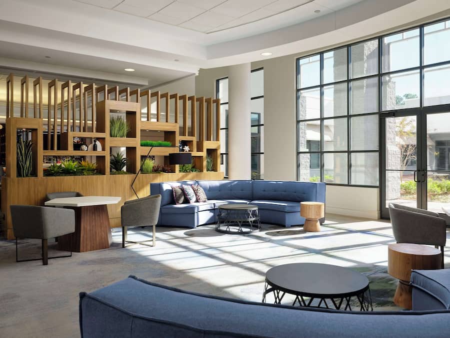 A modern lounge area with a blue sofa, round tables, and a wooden partition with greenery.