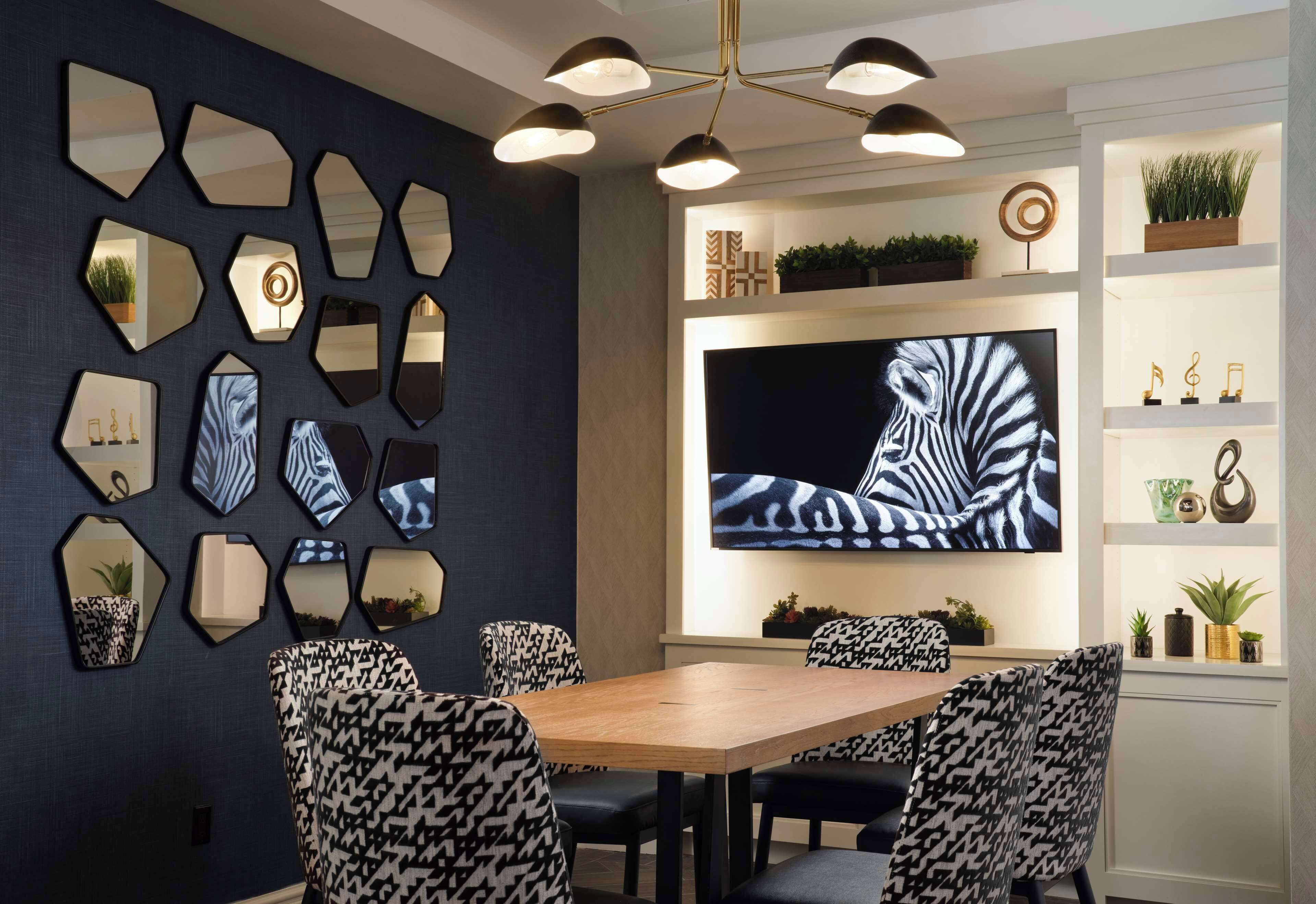 A dining area with a wooden table and patterned chairs, surrounded by hexagonal mirrors and a large zebra-print artwork.