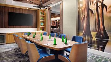 A conference room with a large table, blue chairs, a flat-screen TV, and a mural of trees.