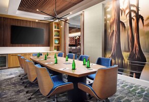 A conference room with a large table, blue chairs, a flat-screen TV, and a mural of trees.