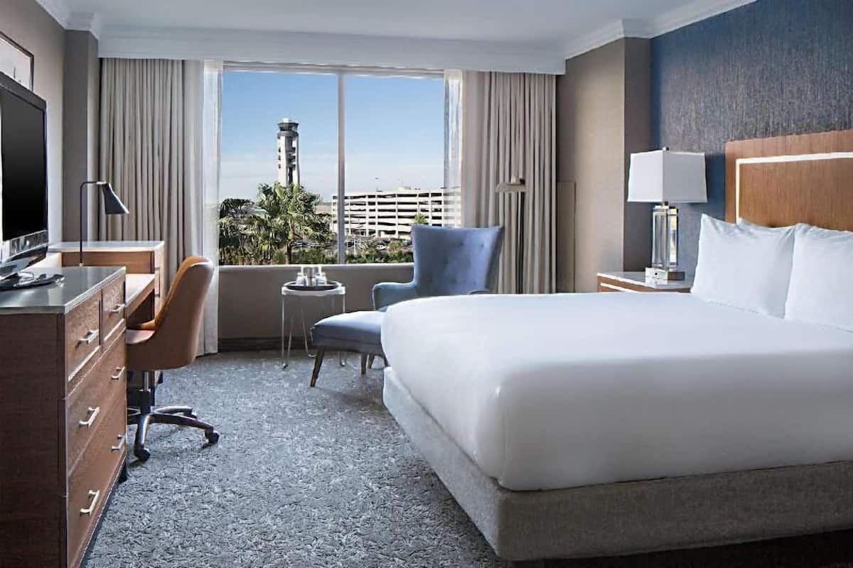 Hotelkamer met een groot bed, een bureau met een televisie, een stoel, een tafeltje en uitzicht op de stad.