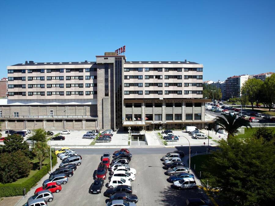 A multi-story hotel with a central tower, parking lot, and surrounding greenery.