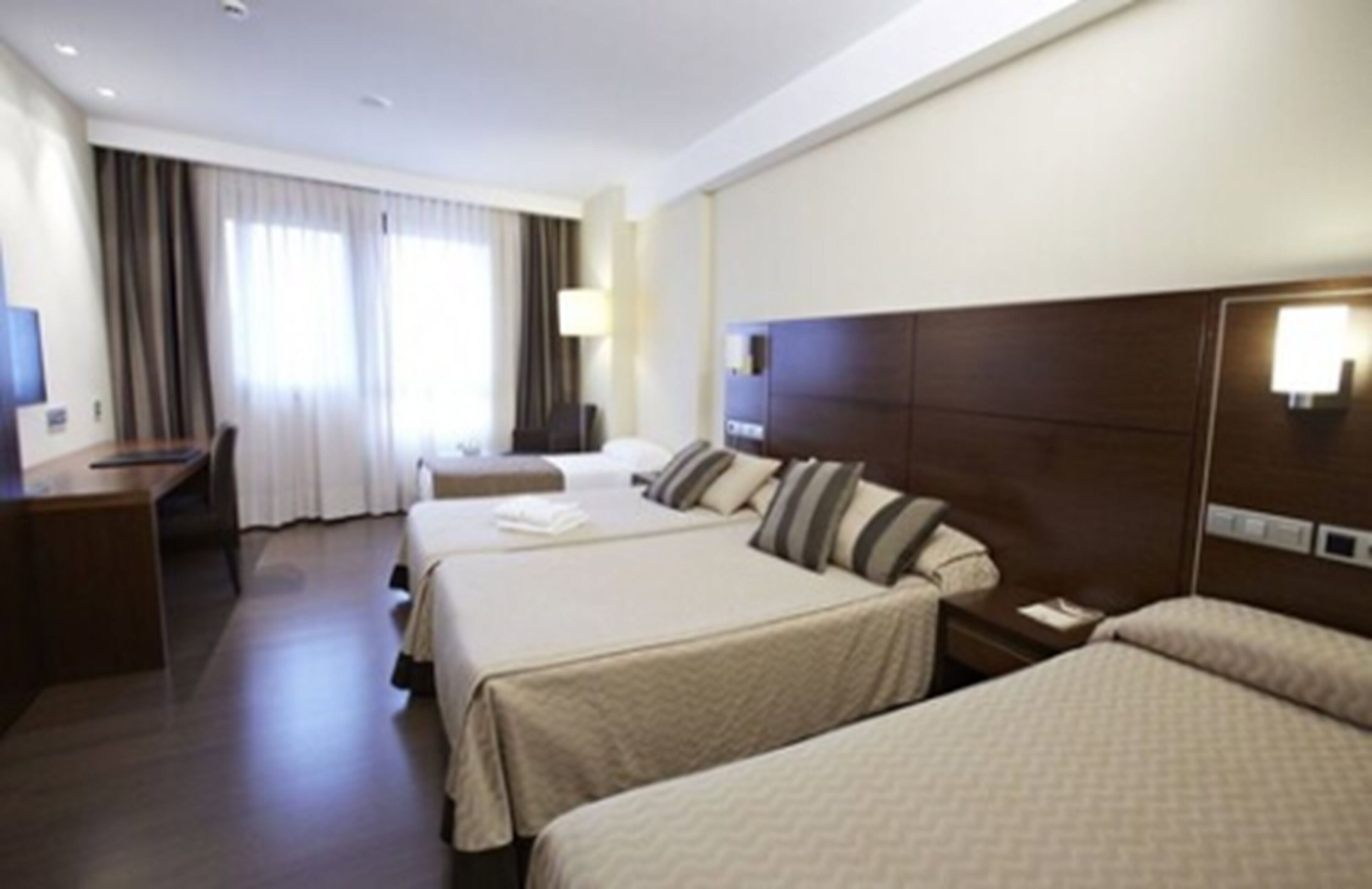 A hotel room with two beds, a desk, and a chair.