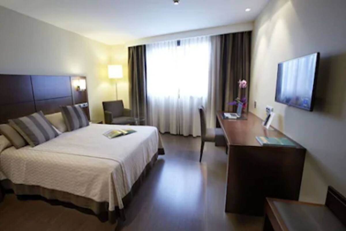 Een hotelkamer met een groot bed, een bureau, een stoel, een televisie en een raam met gordijnen.