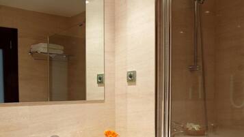 A modern bathroom with a glass-enclosed shower, a sink with a mirror above it, and a small trash bin.