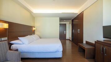 A modern hotel room with a large bed, a wooden headboard, a TV, and a desk.