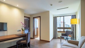 A modern hotel room with a wooden desk, a comfortable sofa, a glass coffee table, and a TV.