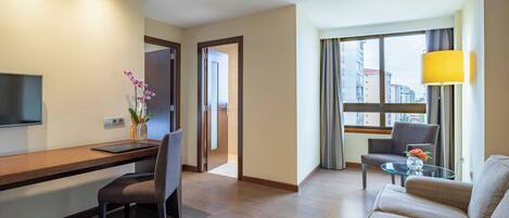 Una habitación de hotel moderna con un escritorio de madera, un sofá cómodo, una mesa de centro de vidrio y un televisor.