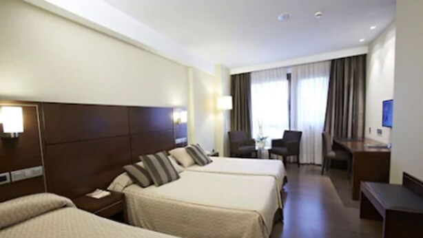 A hotel room with two beds, a desk, a chair, and a television.