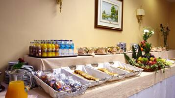 A buffet setup with various food items, beverages, and a framed landscape painting on the wall.