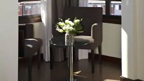 A corner room with a view of the sea, a round table with a vase of flowers, and two chairs.