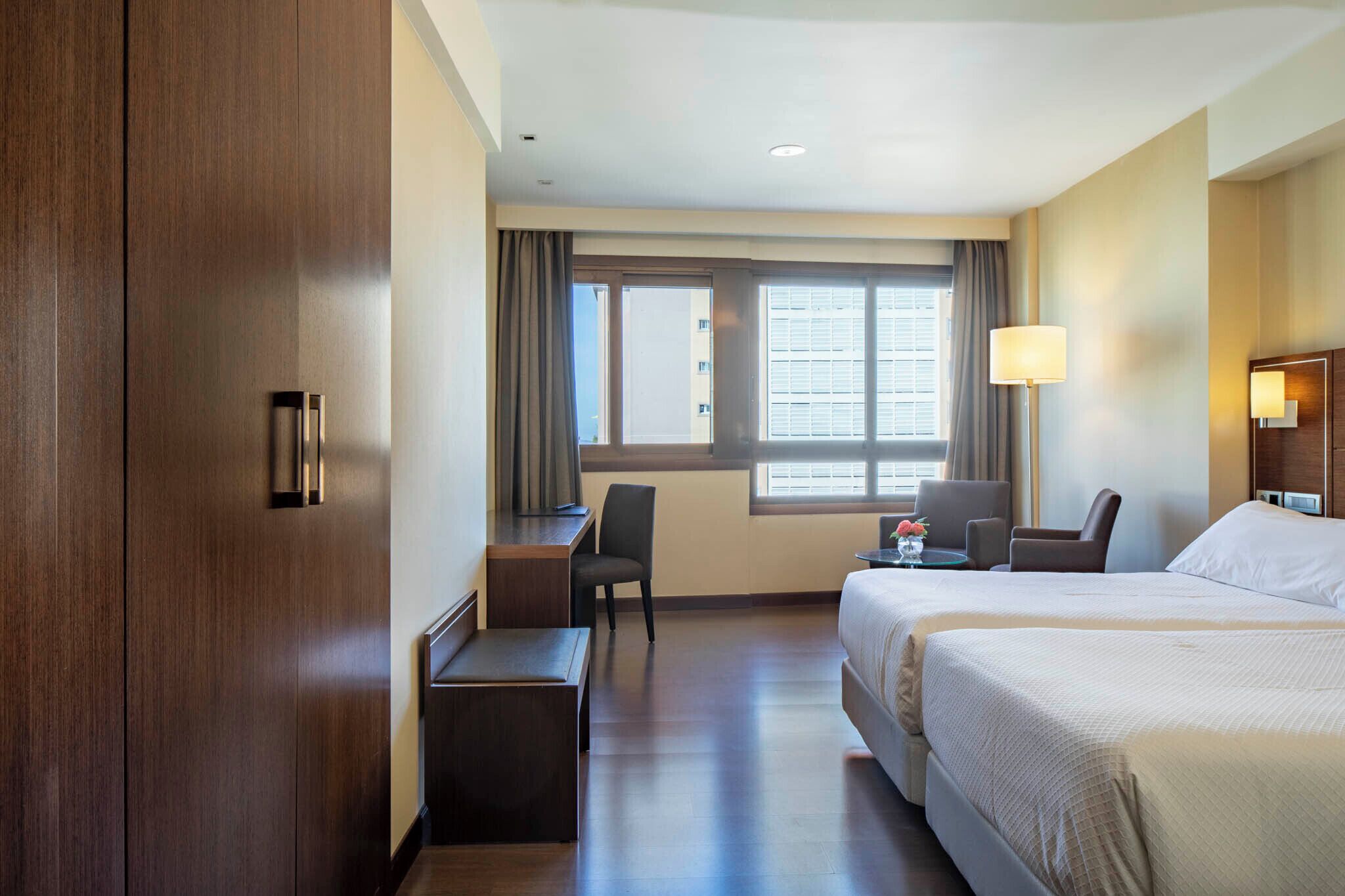 A hotel room with two beds, a desk, a chair, and a window with curtains.