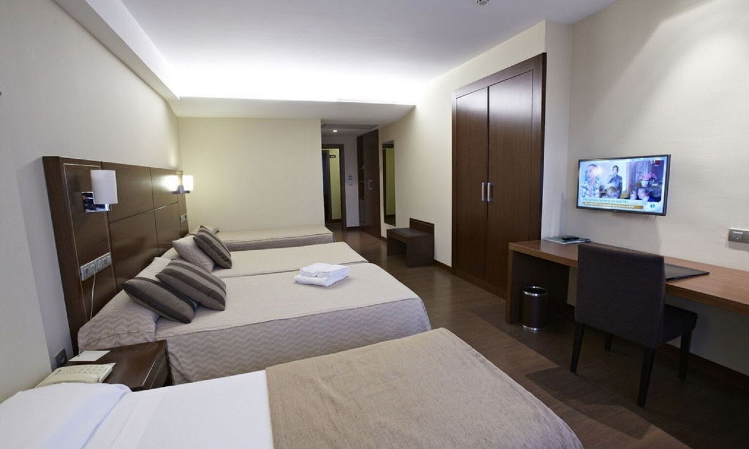 Habitación de hotel con dos camas, un escritorio, una silla, un televisor y un armario.