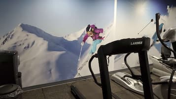 Un gimnasio con cinta de correr, bicicleta estática y un mural de un esquiador.