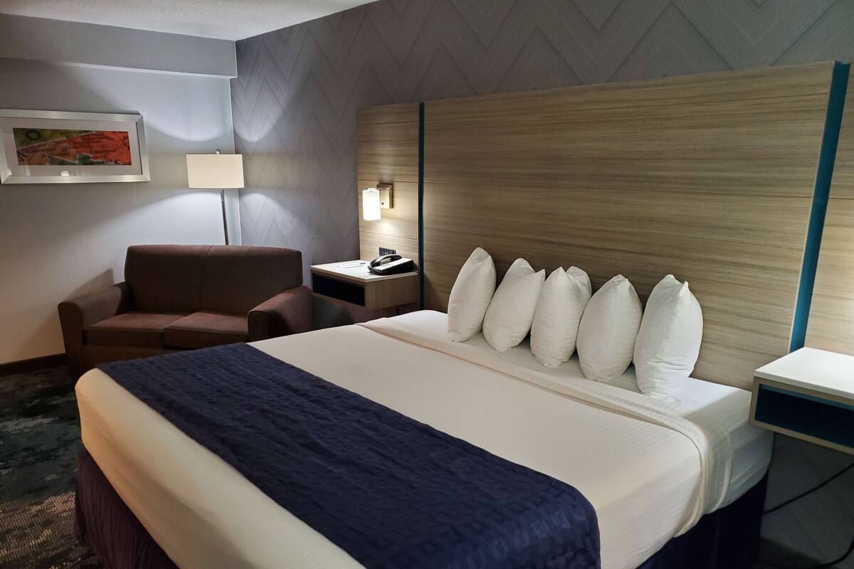 Quarto de hotel com uma cama grande, um sofá, uma escrivaninha com abajur e um telefone fixado na parede.