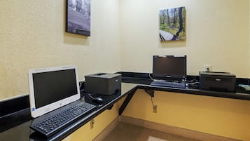A computer desk with a desktop computer, a laptop, and a printer. There are two framed pictures on the wall above the desk.