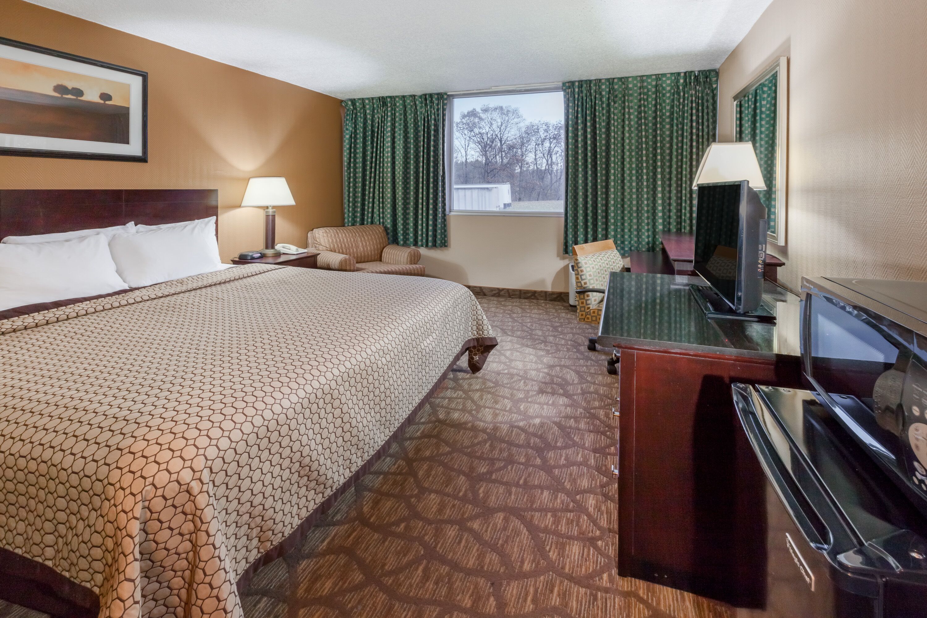Habitación de hotel con una cama grande, un escritorio con una computadora, un televisor y una ventana con cortinas.