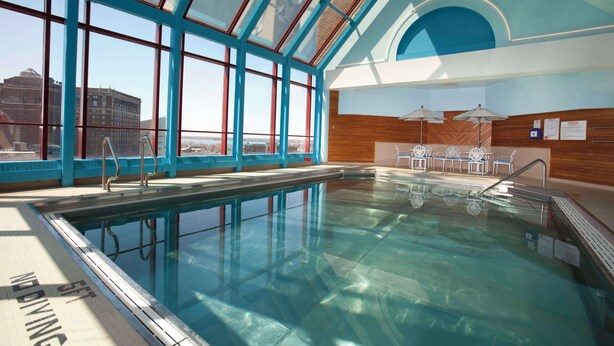 An indoor swimming pool with clear glass walls, a wooden wall, and a view of buildings outside. - Hyatt Regency Buffalo / Hotel and Conference Center (Buffalo)