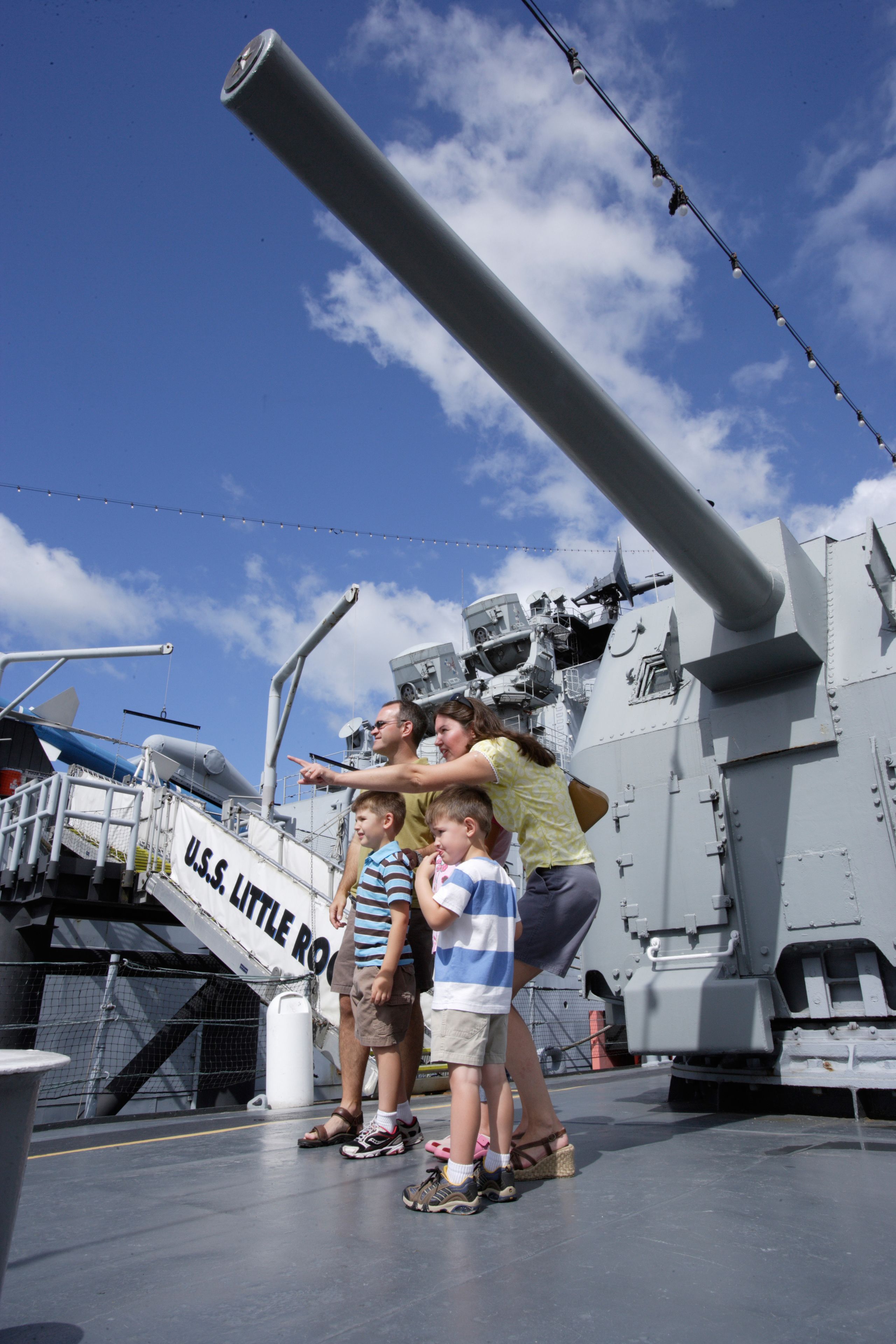 A group of people on a ship deck with a large gun and a sign reading "U.S.S. LITTLE ROCK".
