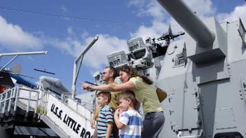 A group of people on a ship deck with a large gun and a sign reading "U.S.S. LITTLE ROCK".
