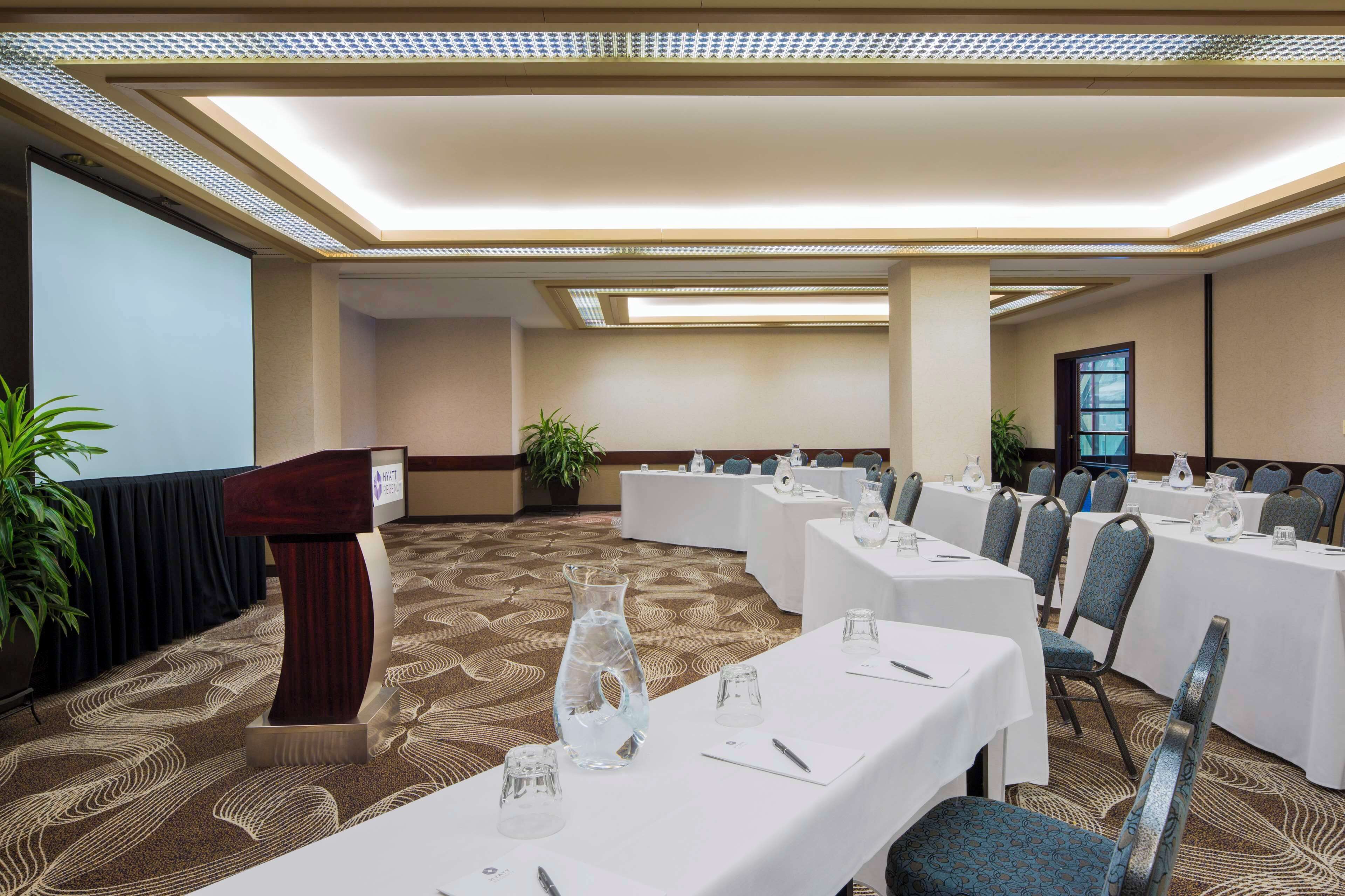 A conference room with tables set for a meeting, a podium, and a large plant.