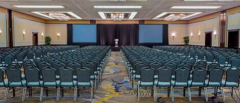 A conference room with rows of chairs, a large screen at the front, and a carpeted floor with a geometric pattern.