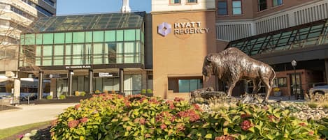 Ein Hyatt Regency Hotel mit großzügigem Eingang, einer Bullstatue und einem angelegten Garten mit verschiedenen Pflanzen.