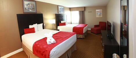 A hotel room with two beds, a desk, a chair, a TV, and a trash can.