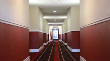 A hallway with red walls and a striped carpet leading to a door at the end.