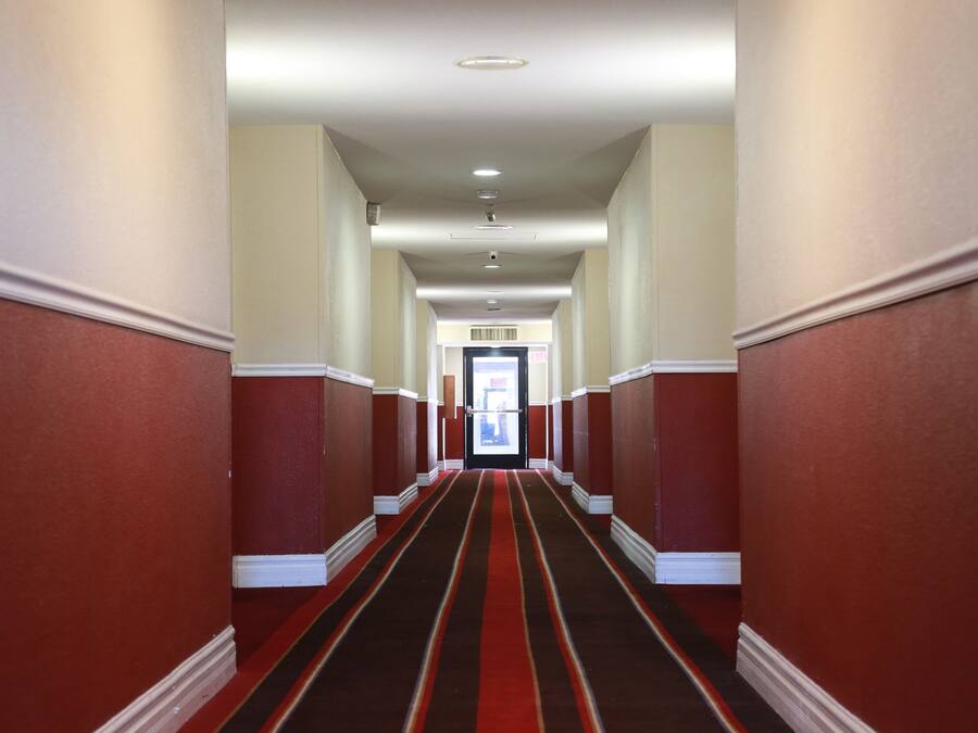 A hallway with red walls and a striped carpet leading to a door at the end.