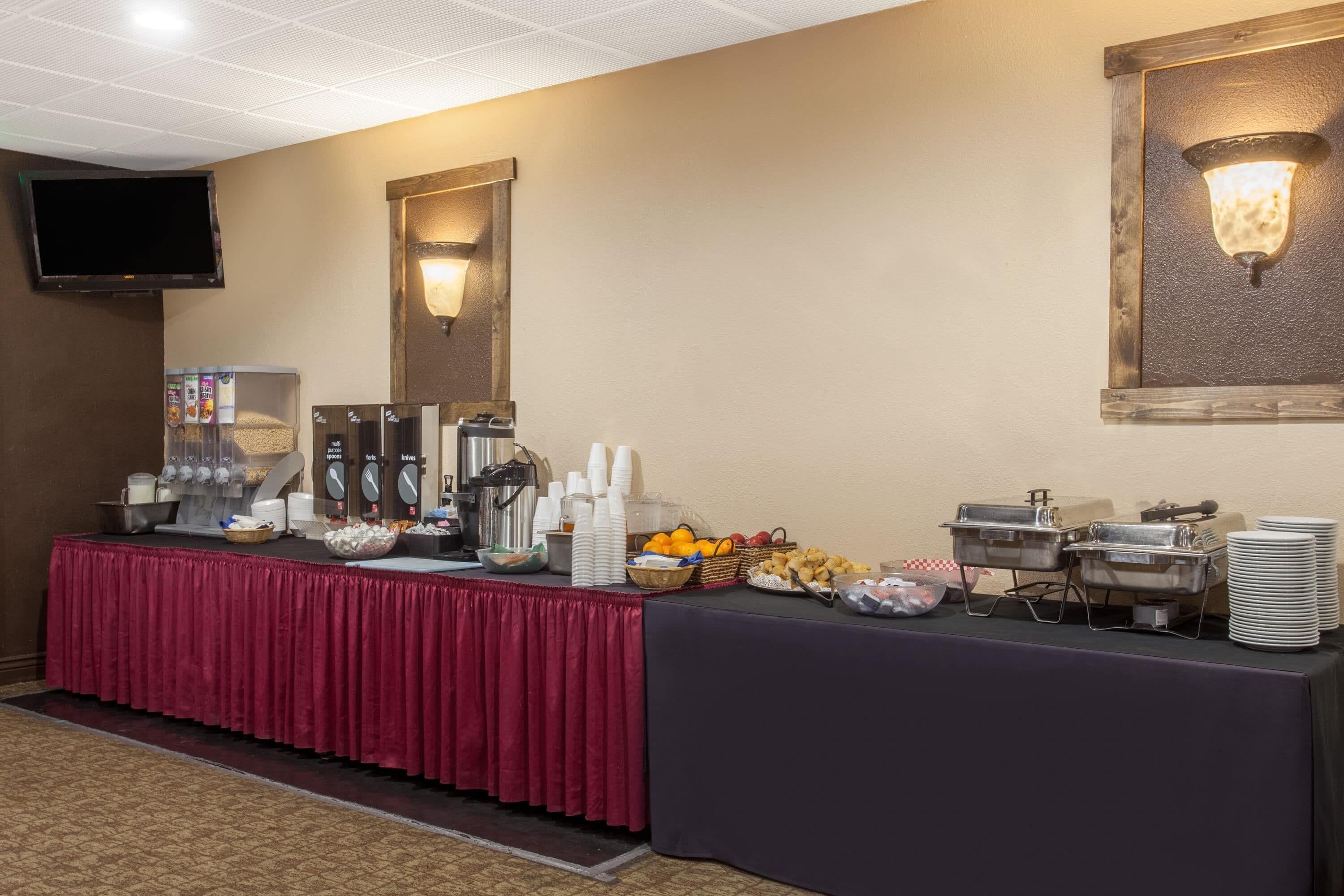 A buffet setup with various food items and beverages, a television mounted on the wall, and a decorative wall light.