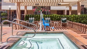 Ein Schwimmbecken mit Metallleiter, umgeben von einer Pflasterterrasse und einem überdachten Sitzbereich mit Stühlen und einem Tisch.
