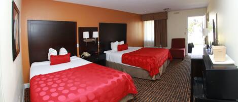 A hotel room with two beds, each with a red polka dot bedspread, a dark headboard, and a nightstand with a lamp.