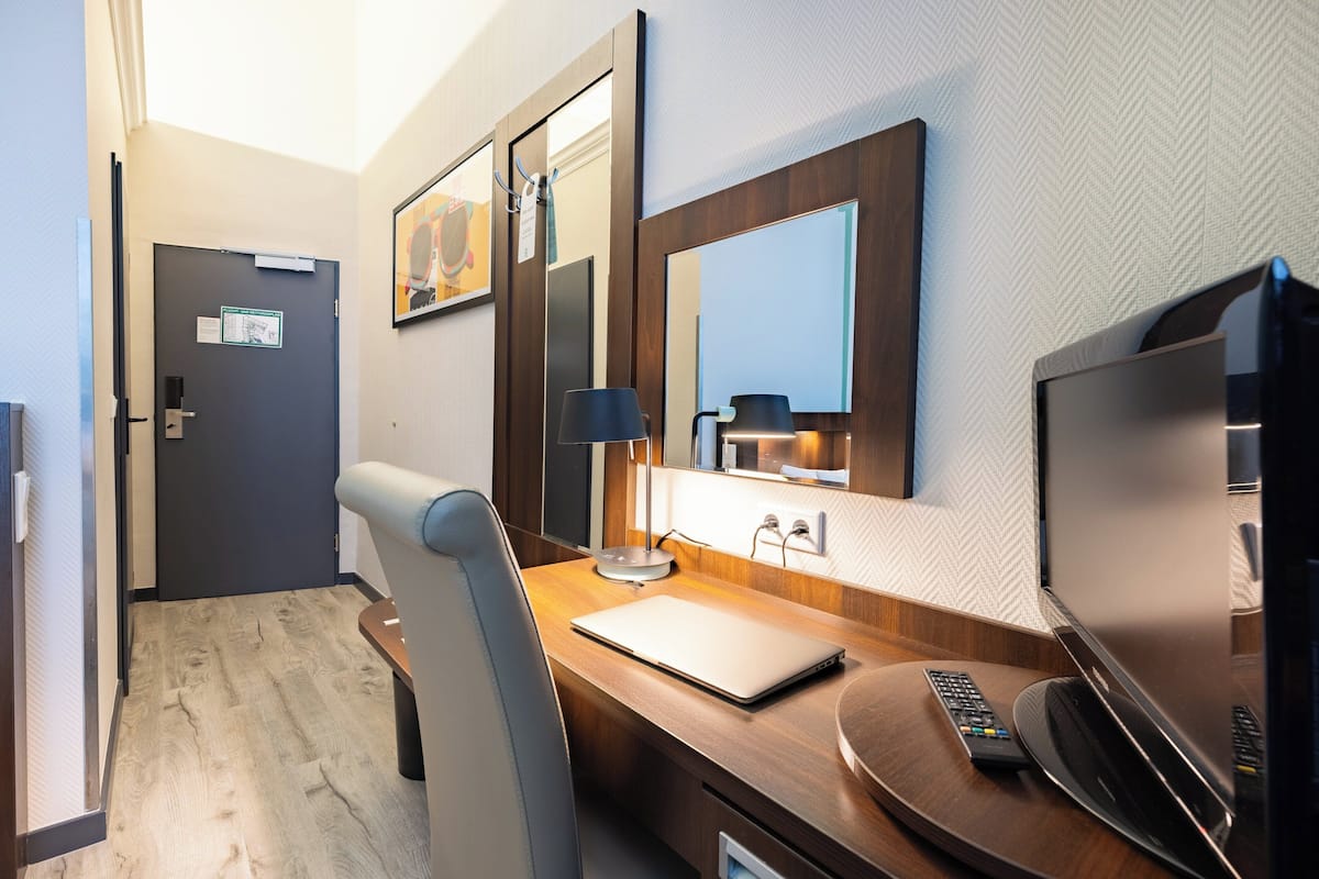 A hotel room with a wooden desk, a laptop, a television, a chair, and a door with a sign.