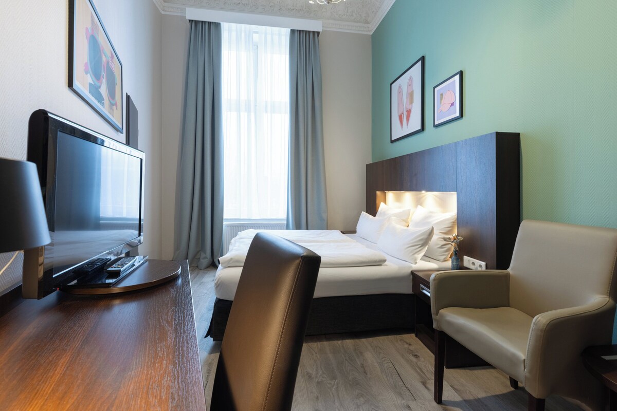 Habitación de hotel con cama, escritorio, ordenador, silla y televisor.