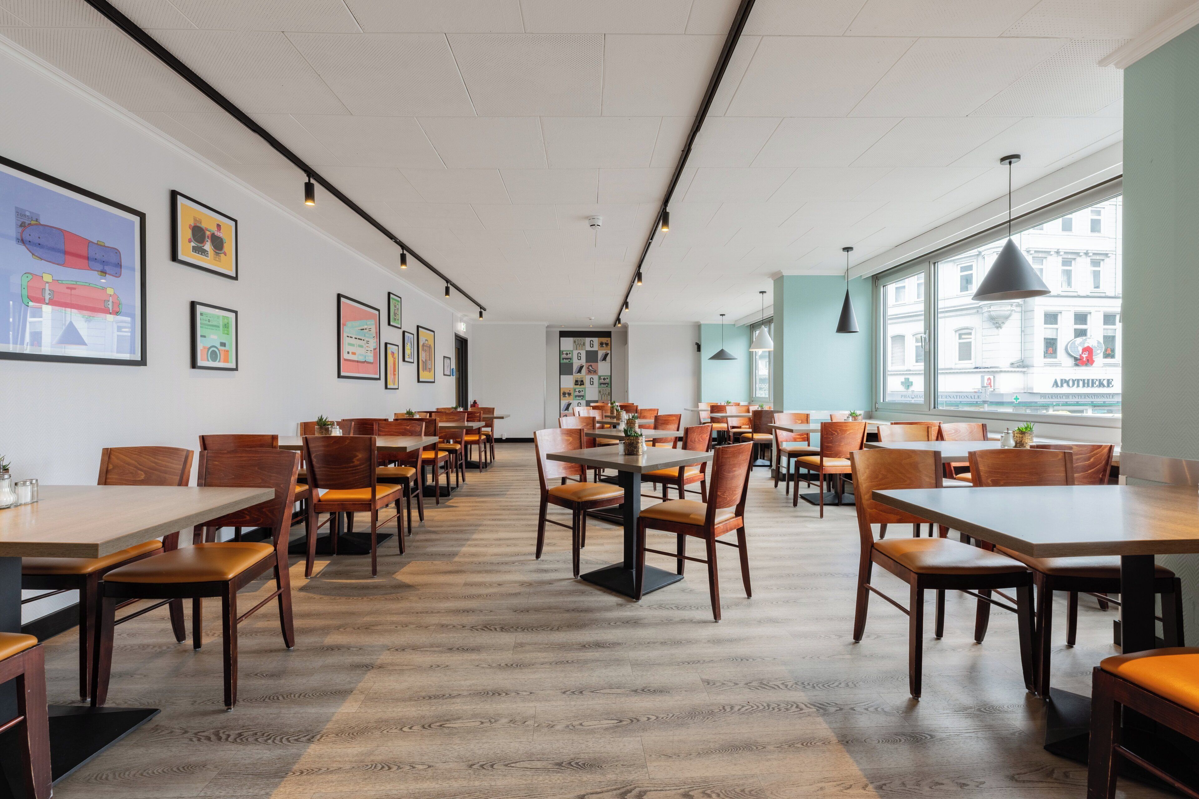 Ein geräumiges Restaurant mit Holztischen und -stühlen, gerahmten Kunstwerken an den Wänden und großen Fenstern mit Blick auf die Stadt.