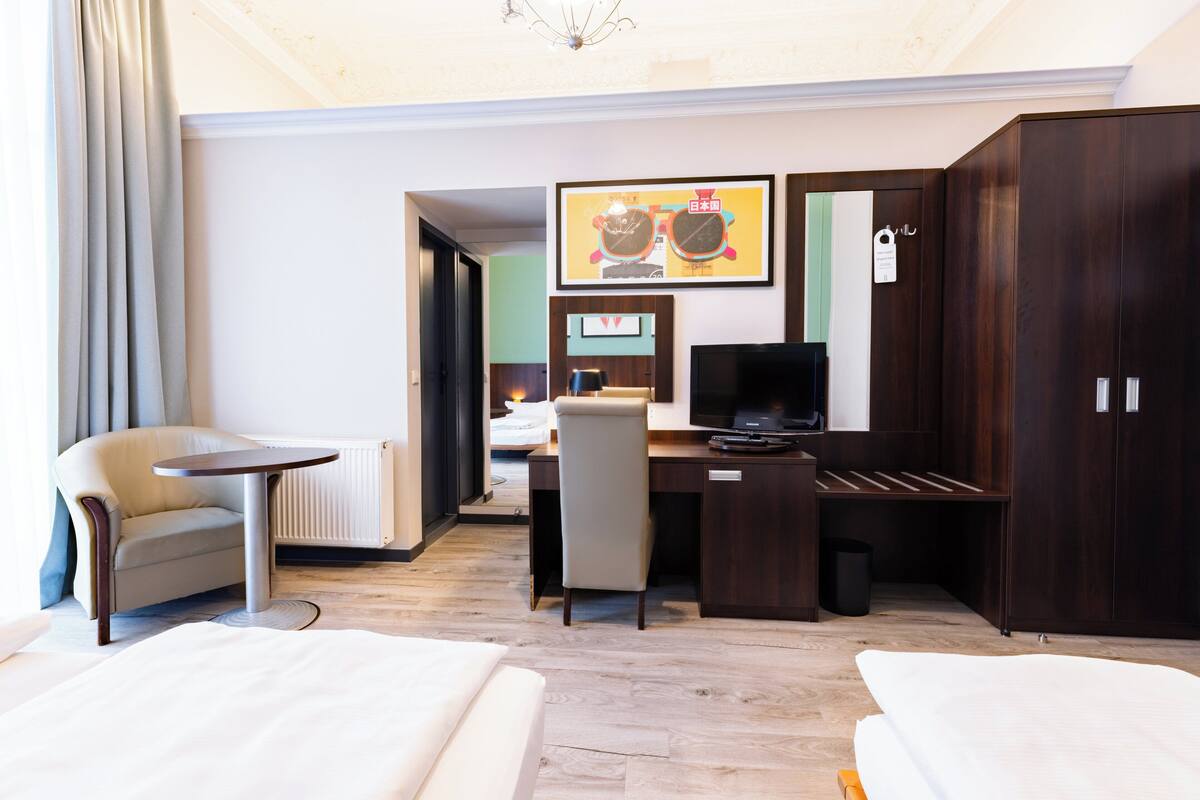 A hotel room with a bed, a desk, a chair, a television, and a wardrobe.