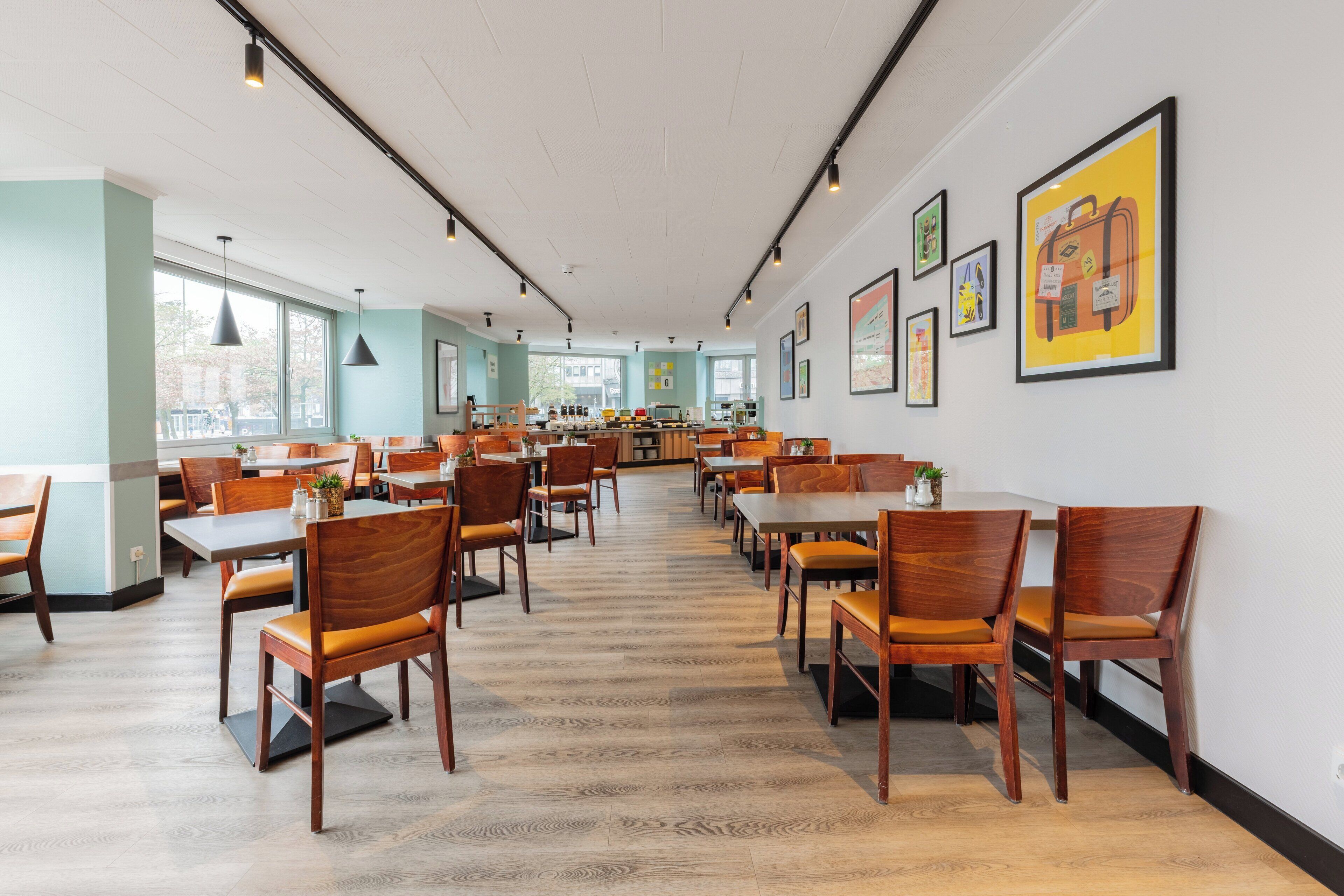 A spacious restaurant with wooden chairs and tables, large windows, and framed artwork on the walls.