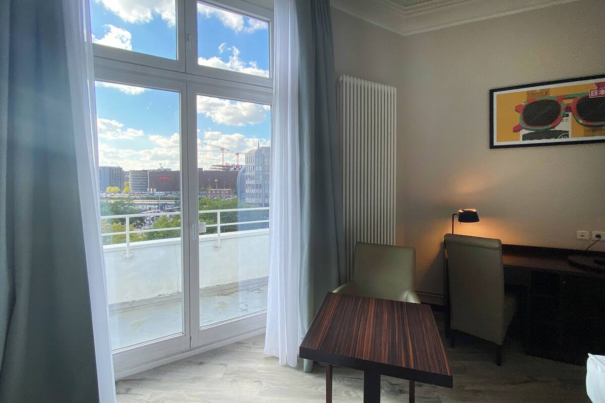 A room with a large window, a table, a chair, and a radiator.