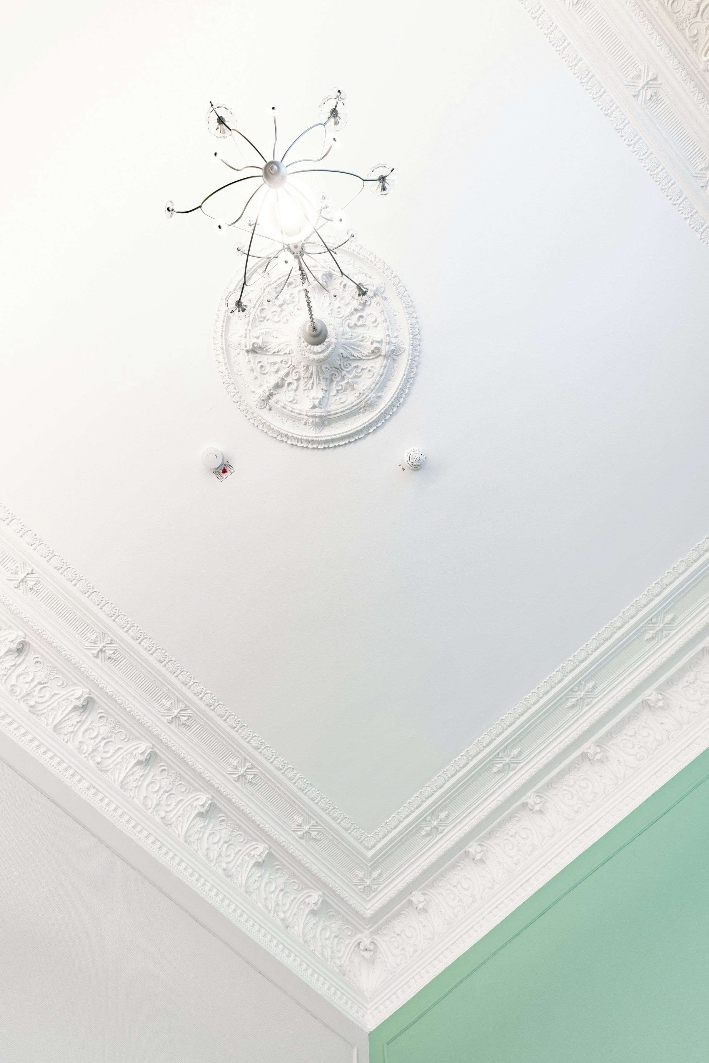 A ceiling with a central chandelier and intricate moldings.