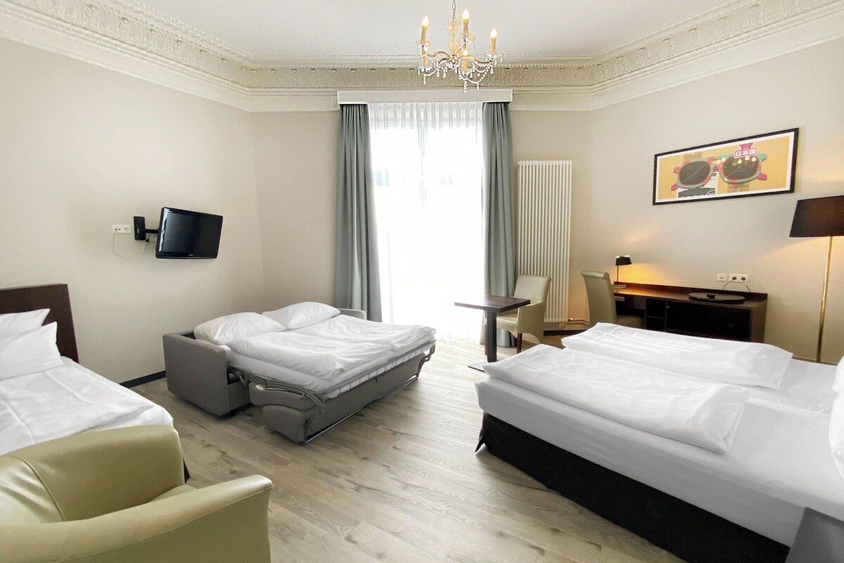 Habitación de hotel con dos camas, un escritorio, una silla, una televisión y un candelabro.