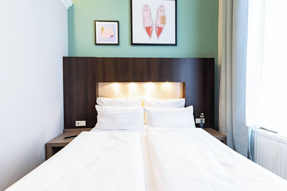 A hotel room with a large bed, two bedside tables, a headboard with integrated lighting, and two framed pictures on the wall.