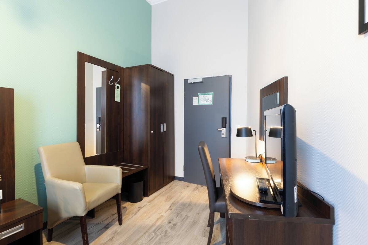 A hotel room with a wooden desk, a chair, a television, and a wardrobe.