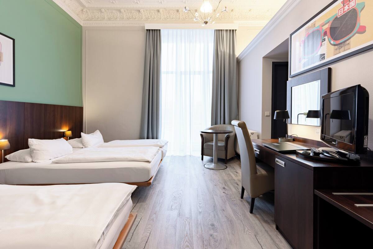Ein Hotelzimmer mit zwei Betten, einem Schreibtisch, einem Stuhl, einem kleinen Tisch und einem Fernseher.