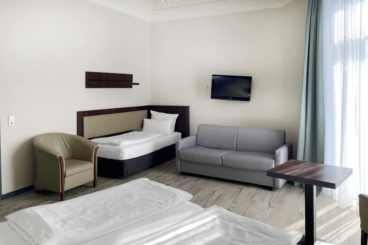 A hotel room with a bed, a sofa, a chair, a TV, and a small table.