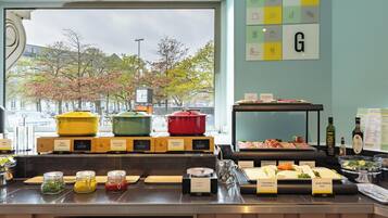 A buffet area with labeled food stations, a view of trees and buildings through a window, and a wall with icons and a letter 'G'.