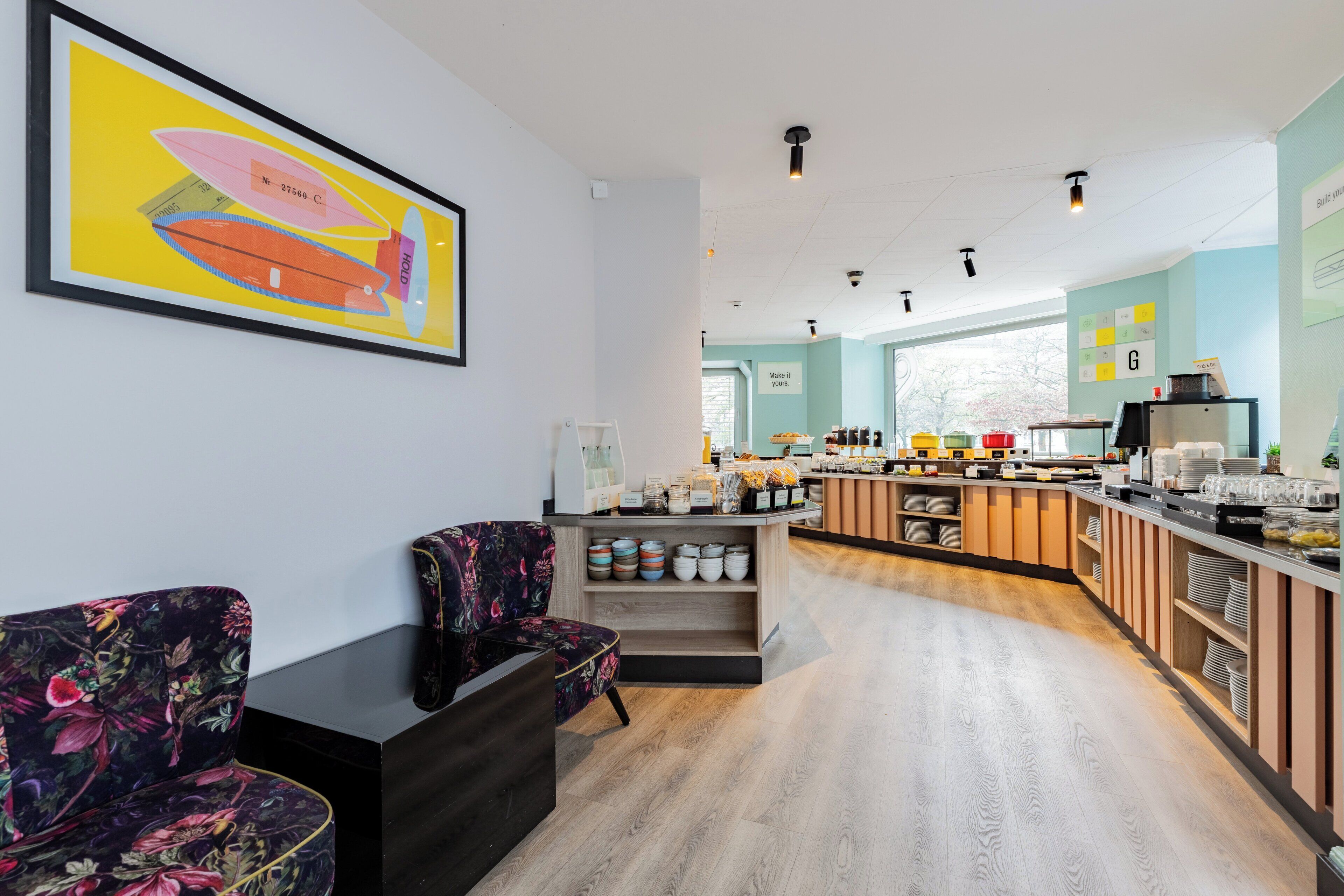 A modern cafe with a wooden counter, seating area, and a large framed artwork on the wall.