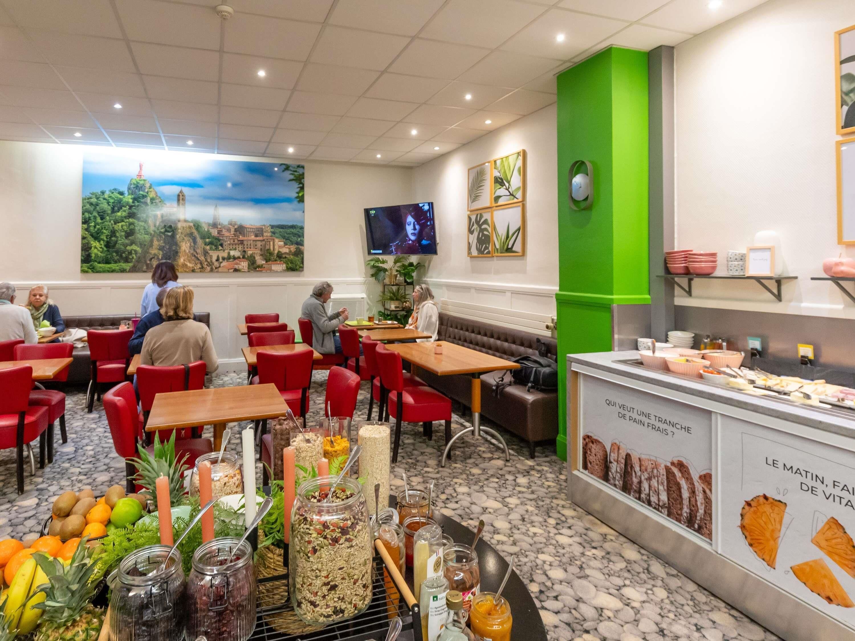 A restaurant with red chairs, a buffet with various food items, a green accent wall, and a large painting of a landscape.