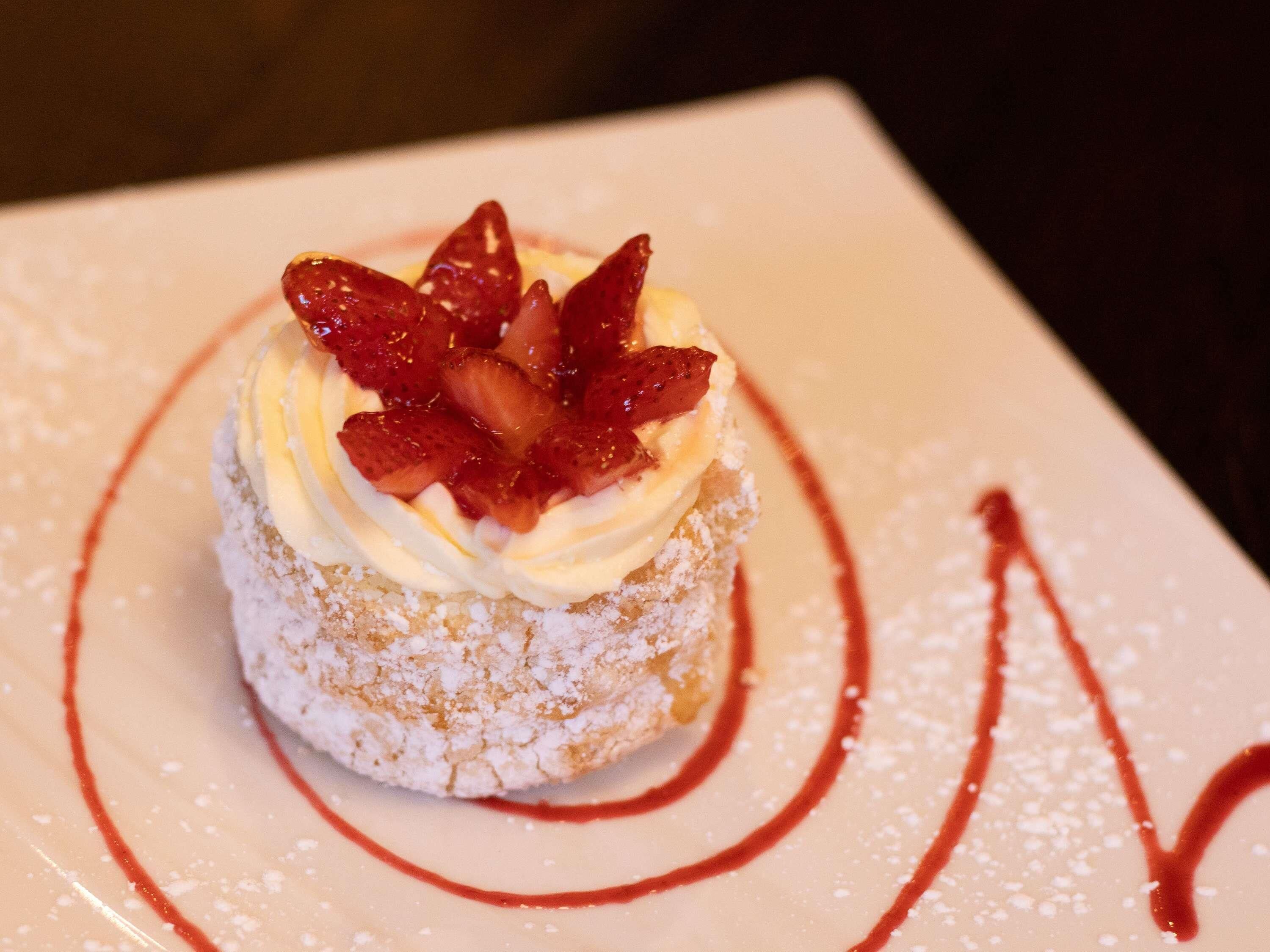 A dessert with whipped cream and strawberries on a powdered sugar-dusted cake.